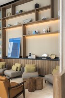 Un área de estar moderna con diversas opciones de asientos, incluyendo sofás y sillones, dispuestos alrededor de mesas de madera.