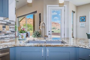 A kitchen with a granite countertop, a stainless steel faucet, and a view of a red rock landscape through a door. - 360° red‑rock views + Full RV hookups in Kanab (Kanab)