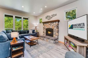 A modern living room with a stone fireplace, a large flat-screen TV, and a comfortable seating area. - Chicken by the Sea by Manzanita Beach Getaway: New Build, Dog-Friendly (Manzanita)
