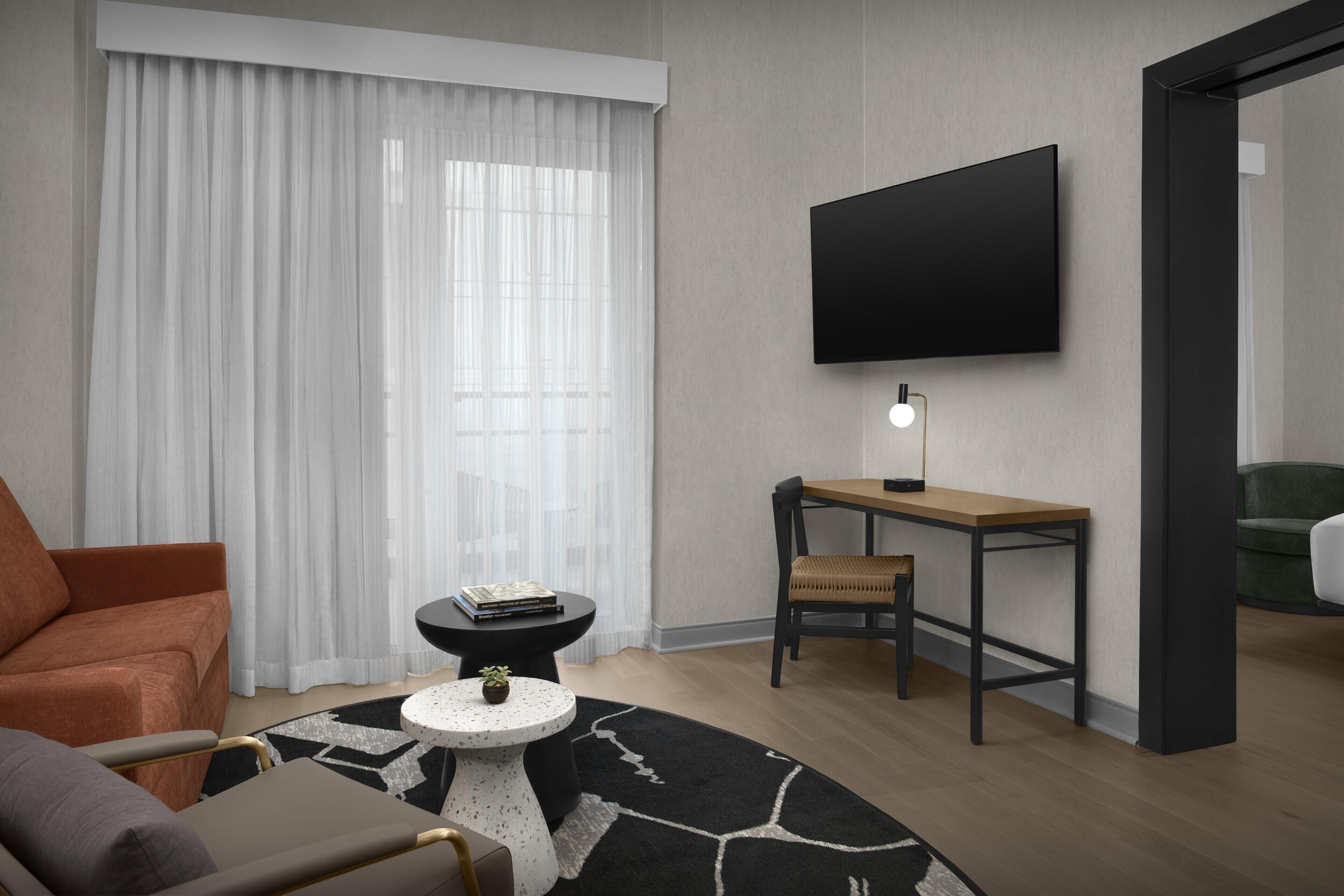Una sala moderna con un sofá, una mesa redonda de centro, una mesita auxiliar con una planta, un televisor de pantalla plana montado en la pared y un sillón verde.