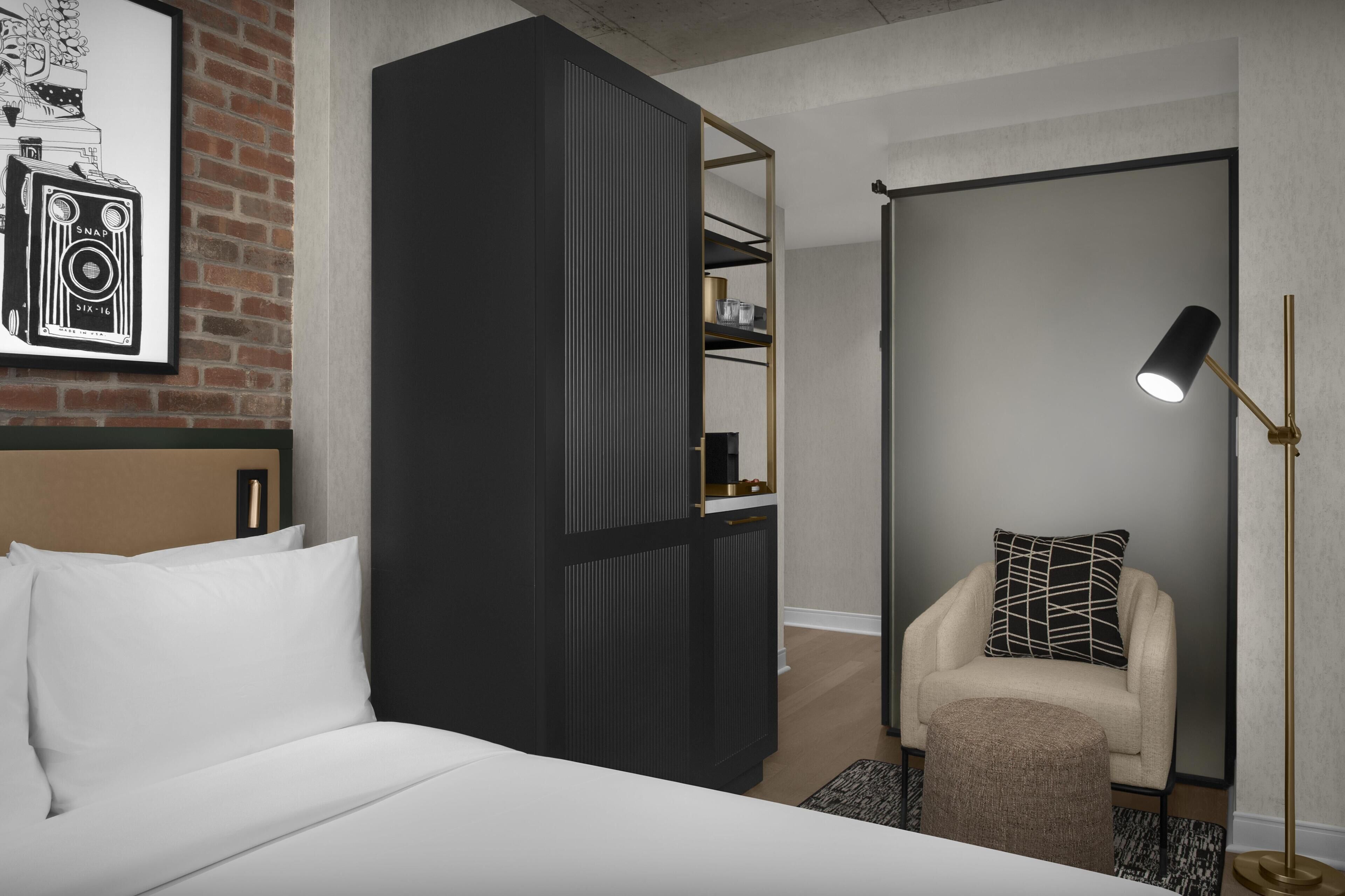 A modern hotel room with a bed, a wardrobe, a chair, and a floor lamp.