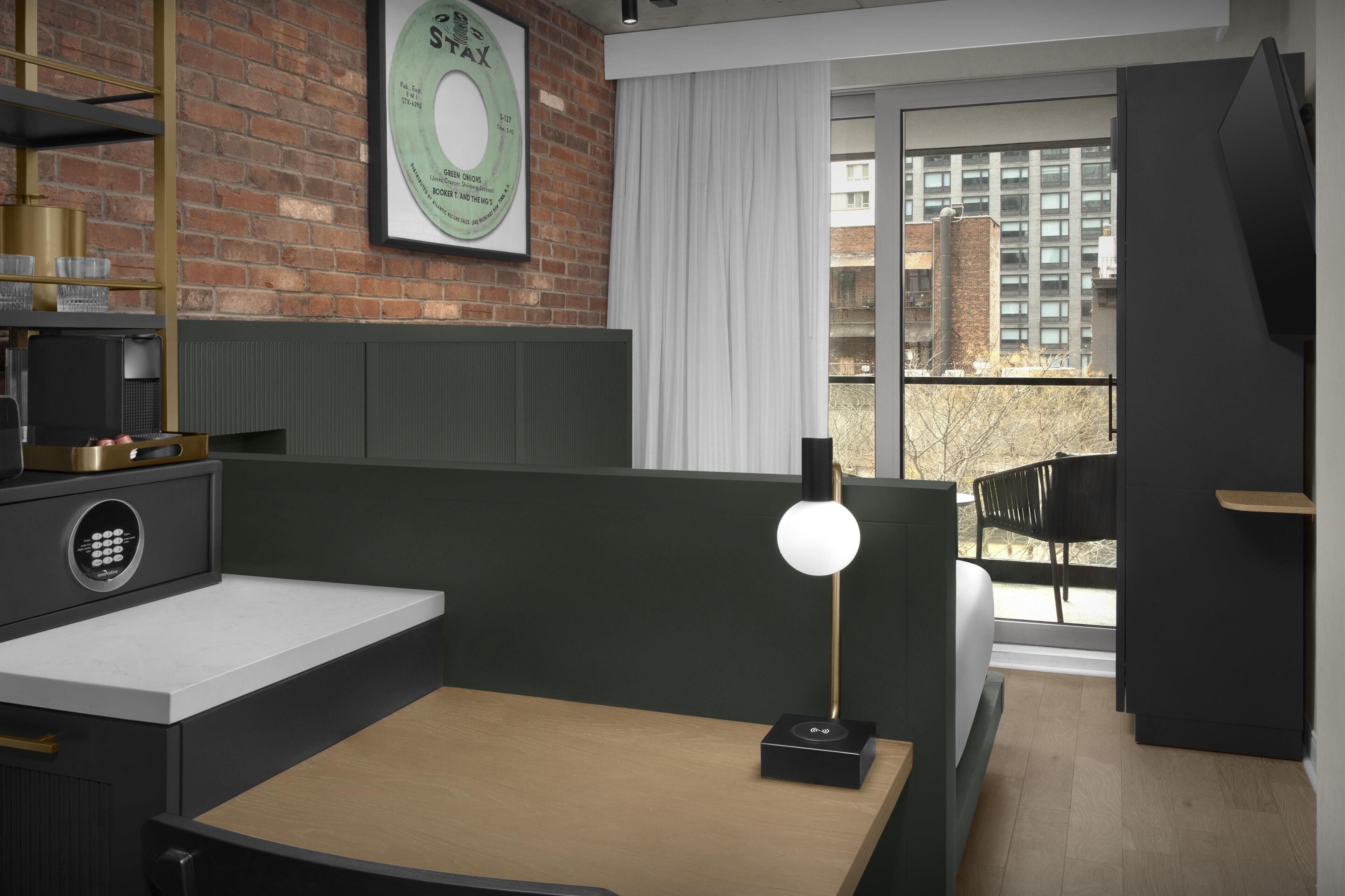 A modern room with a desk, a chair, a window with a view of buildings, and a framed record on the wall.