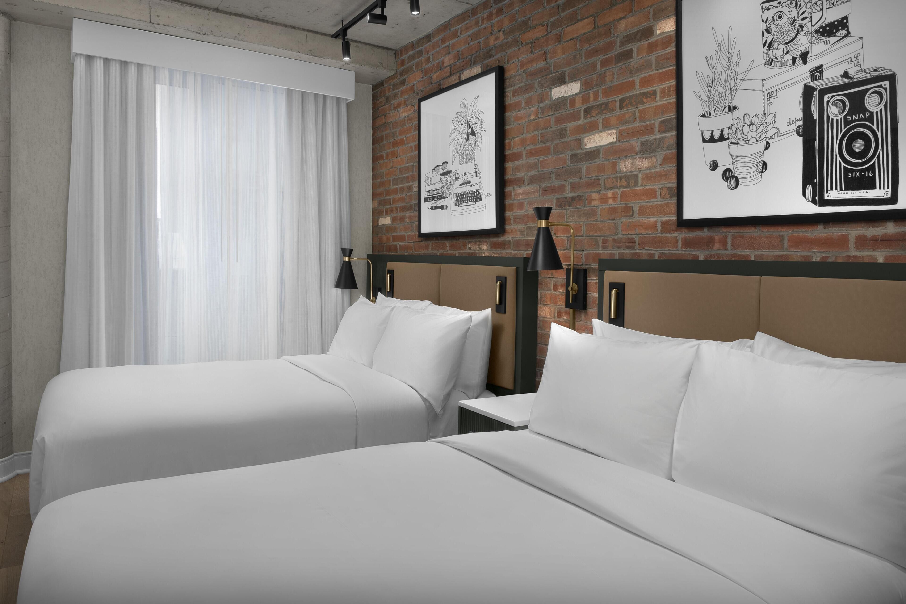 Une chambre d’hôtel avec deux lits, un mur en briques et deux tableaux encadrés.