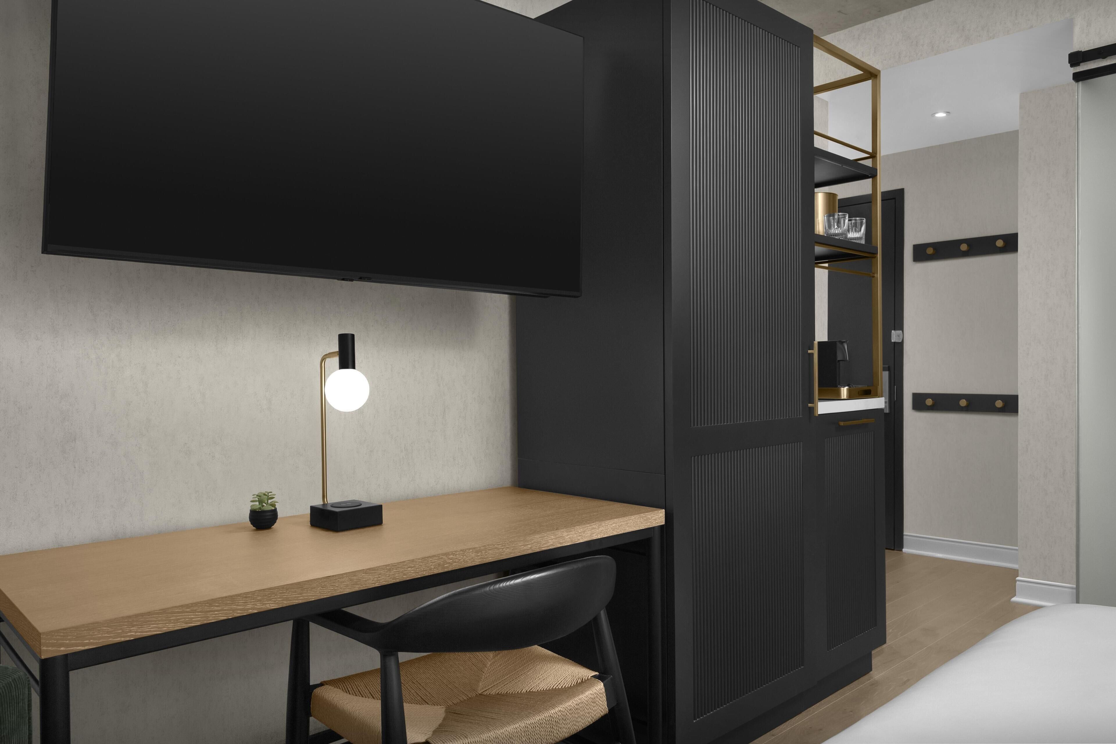 A modern bedroom with a bed, a desk with a chair, a TV mounted on the wall, and a wardrobe with a mirror.