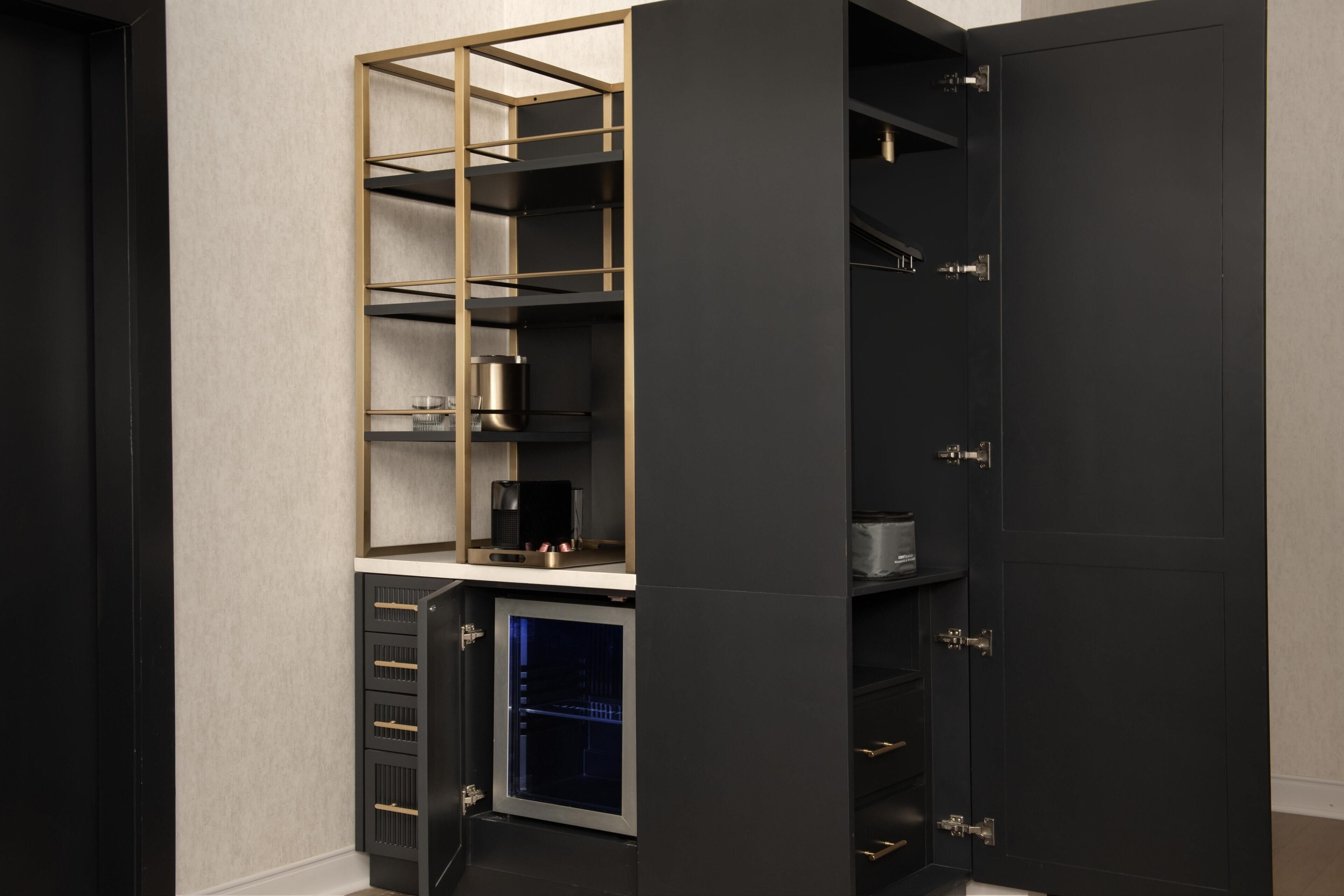 A modern, dark-colored storage unit with multiple shelves and drawers, featuring a built-in coffee machine and a small refrigerator.