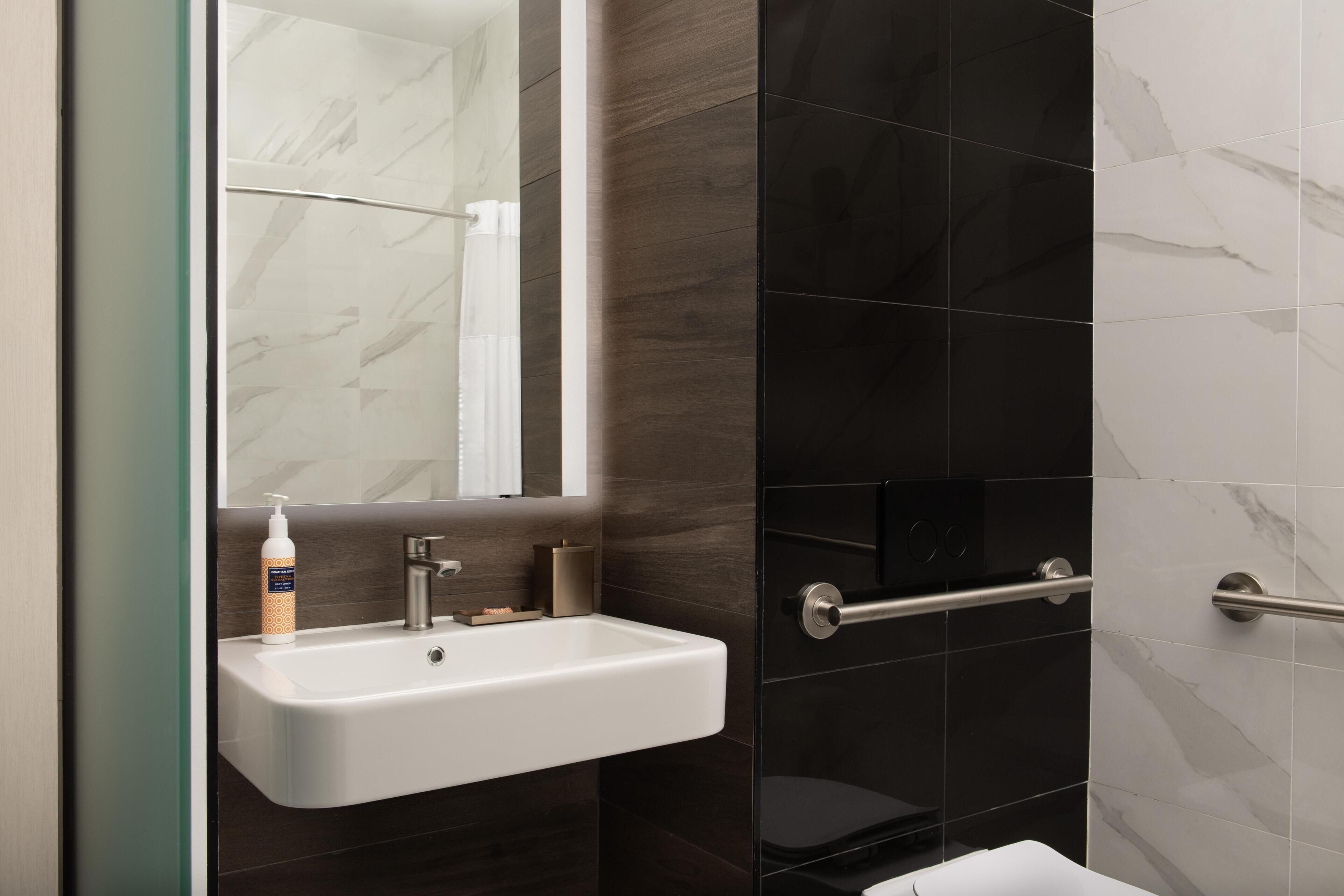 A bathroom with a white sink, a mirror, and dark tiled walls.
