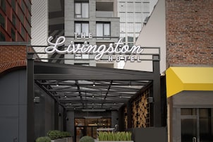 A entrada do Hotel Livingstone, com design moderno, apresentando uma cobertura de vidro e fachada de tijolos.