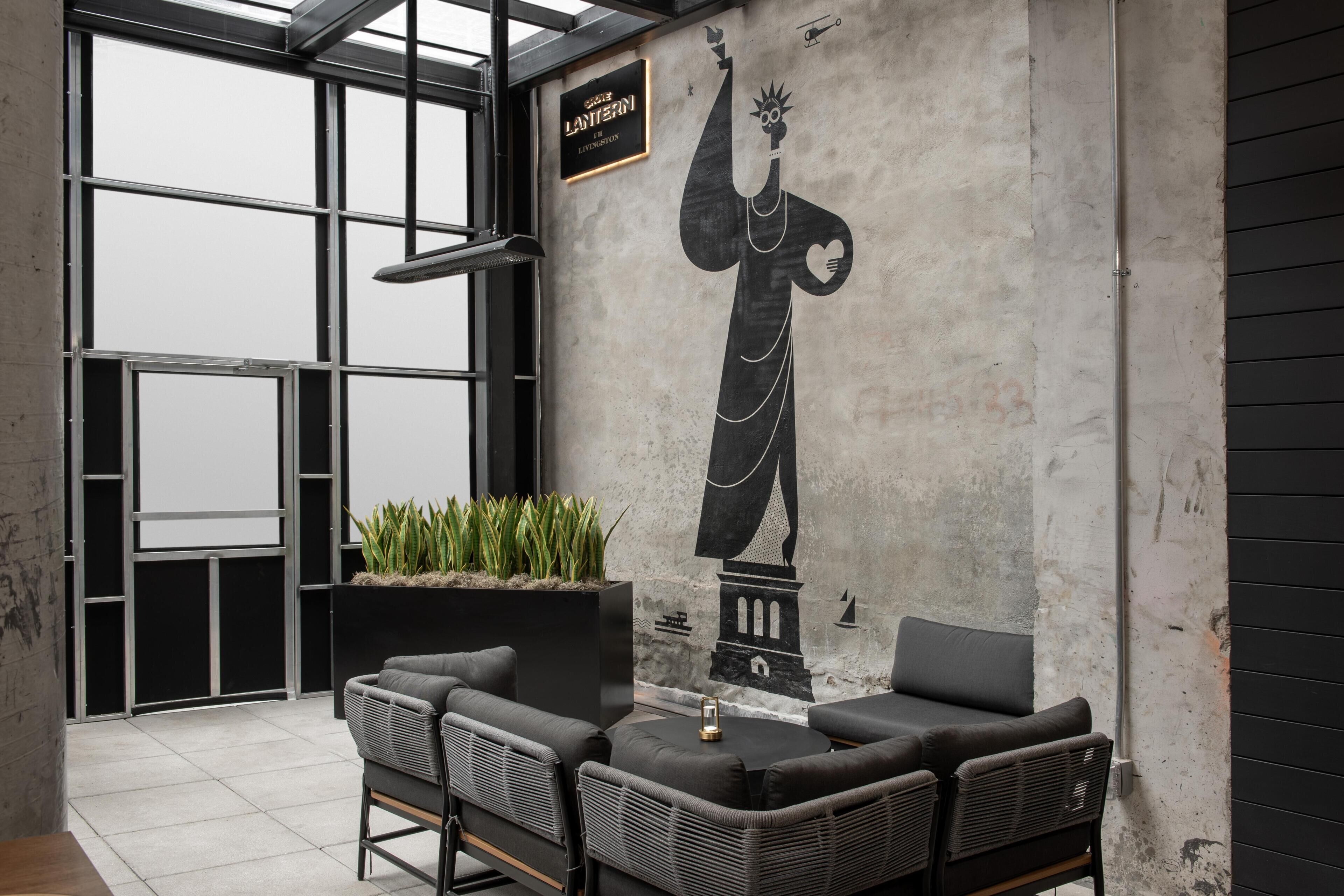 Ein moderner Lounge-Bereich mit einer großen Wandmalerei einer Statue, Sitzgelegenheiten und einem Schild mit dem Namen des Hauses.