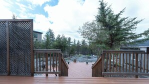 A wooden deck with a view of a forested area and a building in the background.