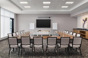 Uma sala de conferências com uma mesa comprida, cadeiras, uma televisão e alto-falantes.