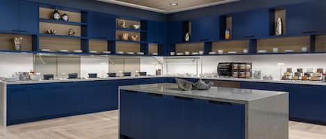 A modern kitchen with blue cabinetry, a central island, and various kitchenware displayed on shelves.