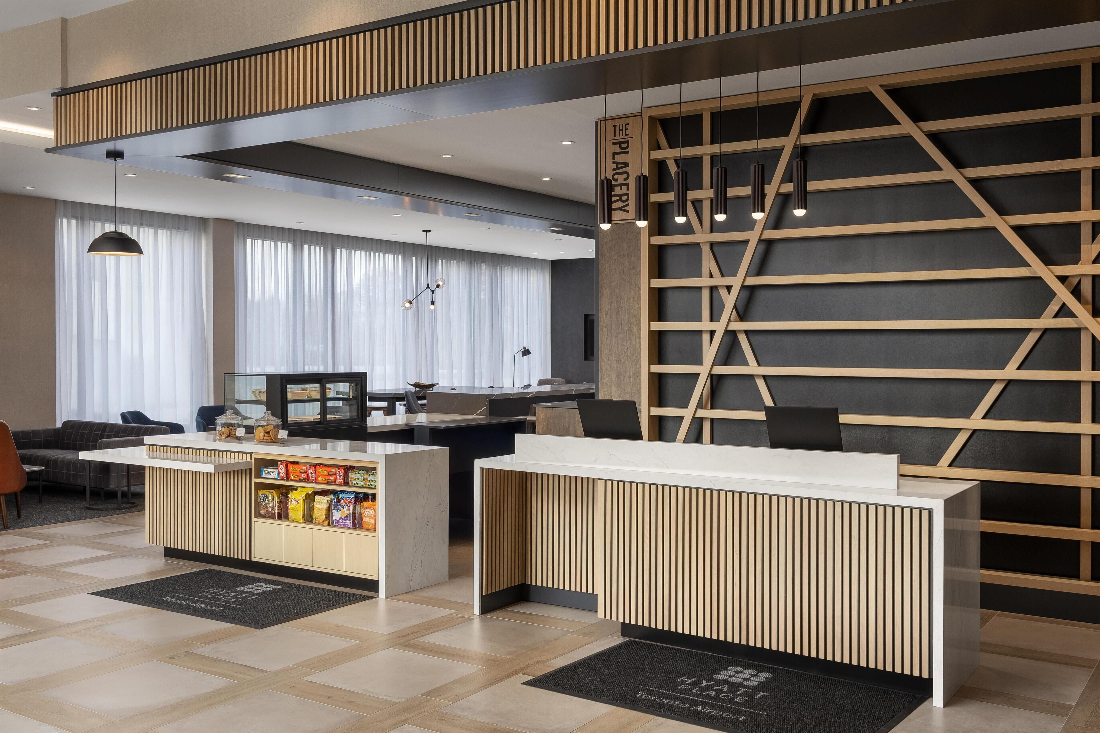 Una zona de recepción moderna con un mostrador de madera, un espacio con aperitivos y un área de descanso con un sofá y sillones.