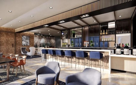 A modern bar area with a long counter, bar stools, and a variety of bottles and glasses.