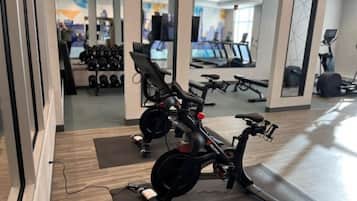 Un gimnasio con bicicletas estáticas, cintas de correr y un espejo que refleja el espacio.