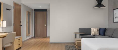 Una habitación de hotel moderna con piso de madera, un escritorio con silla, una cama, un sofá, una mesita y una lámpara colgante.