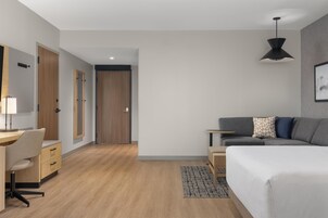 Een moderne hotelkamer met een houten vloer, een bureau met stoel, een bed, een bank, een kleine tafel en een hanglamp.