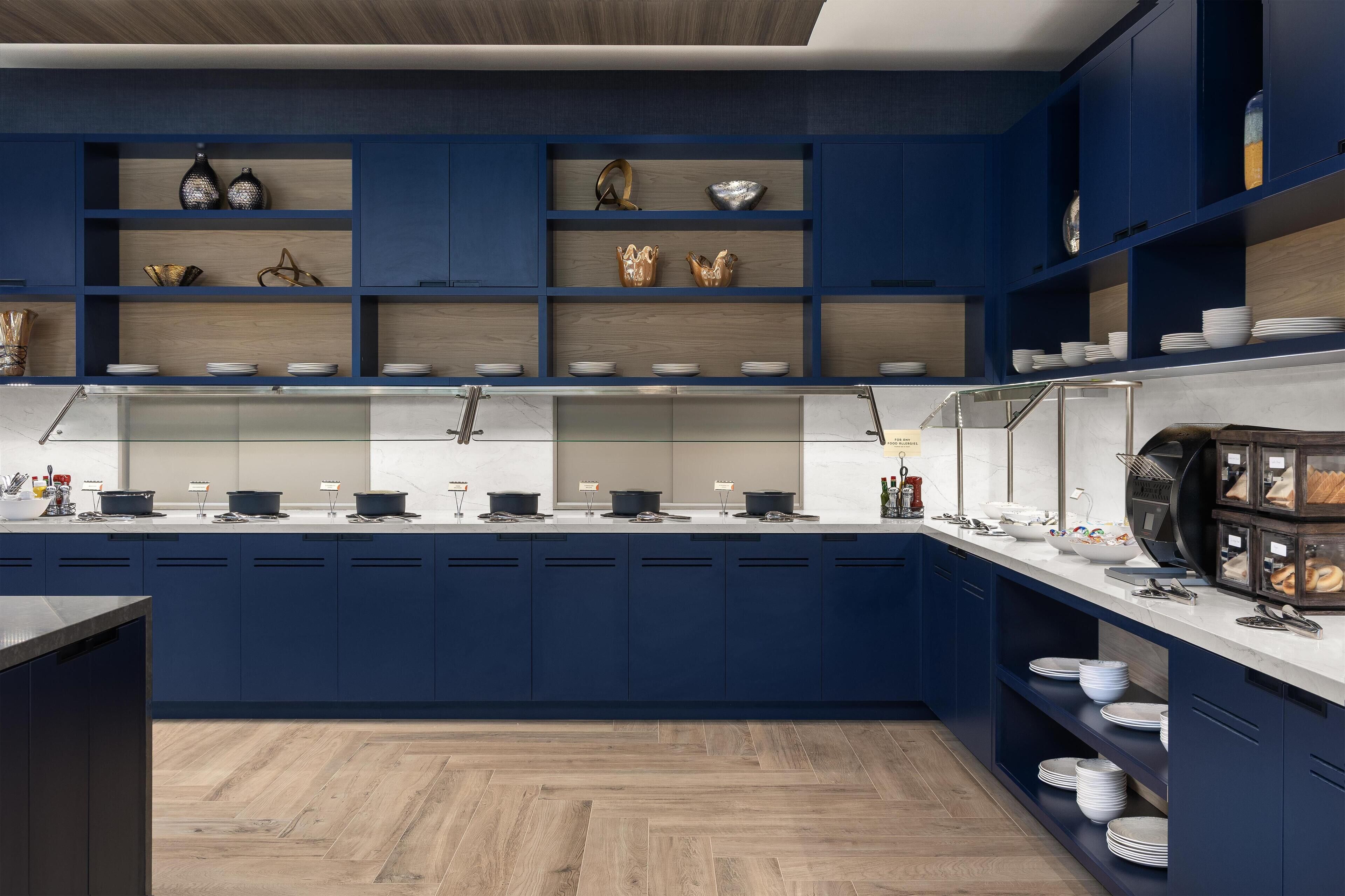 A modern kitchen with dark blue cabinets, wooden shelves, and a marble countertop.