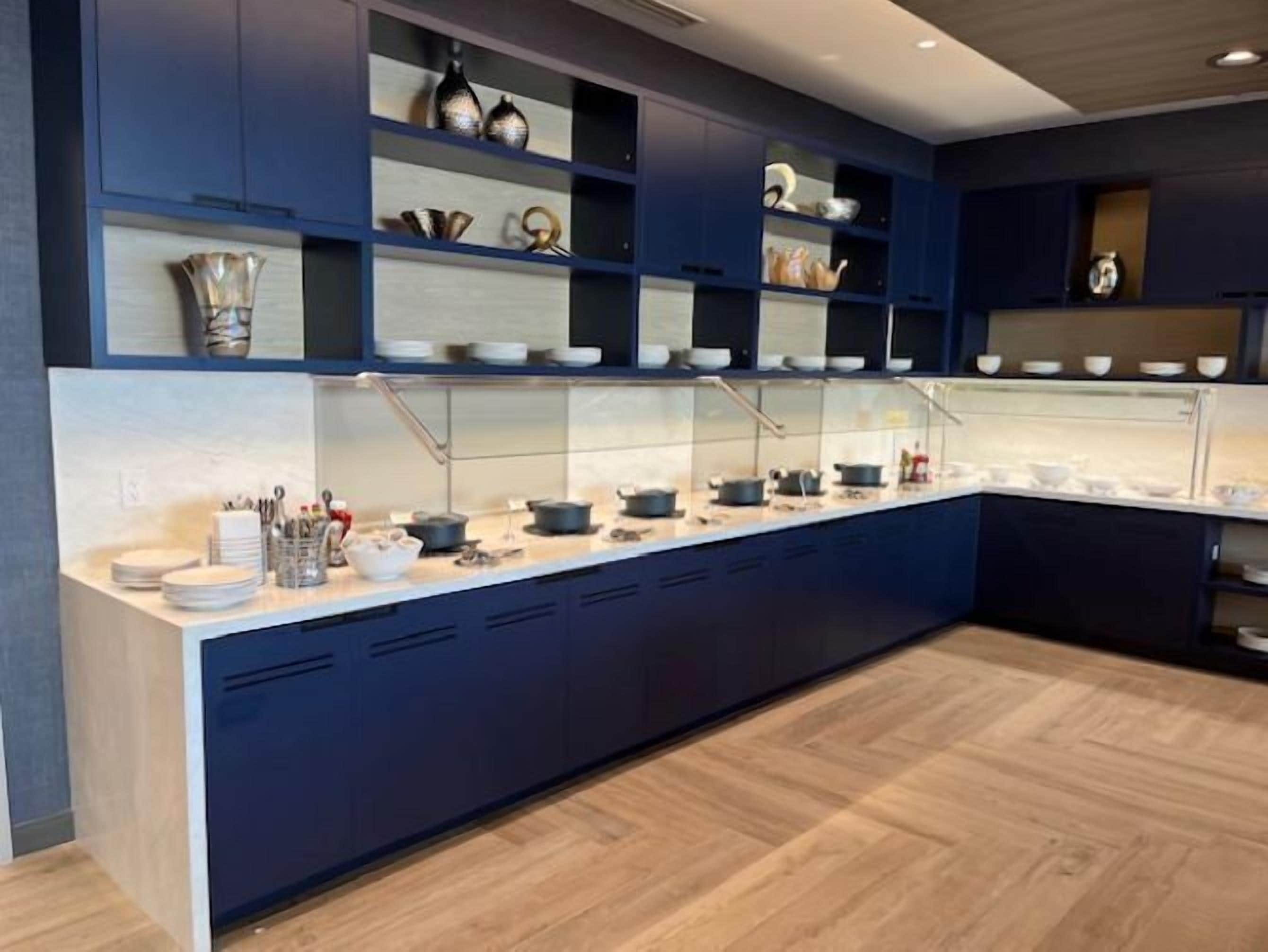 A modern kitchen with blue cabinets, a white countertop, and various kitchenware.
