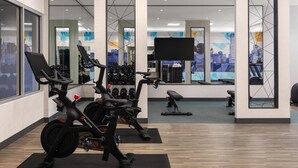A modern gym with stationary bikes, weight machines, and a large TV screen. - Hyatt Place Toronto Airport (TORONTO)