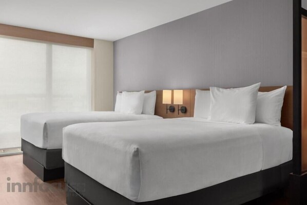 Una habitación de hotel con dos camas, un ventanal grande y una lámpara fijada a la pared.