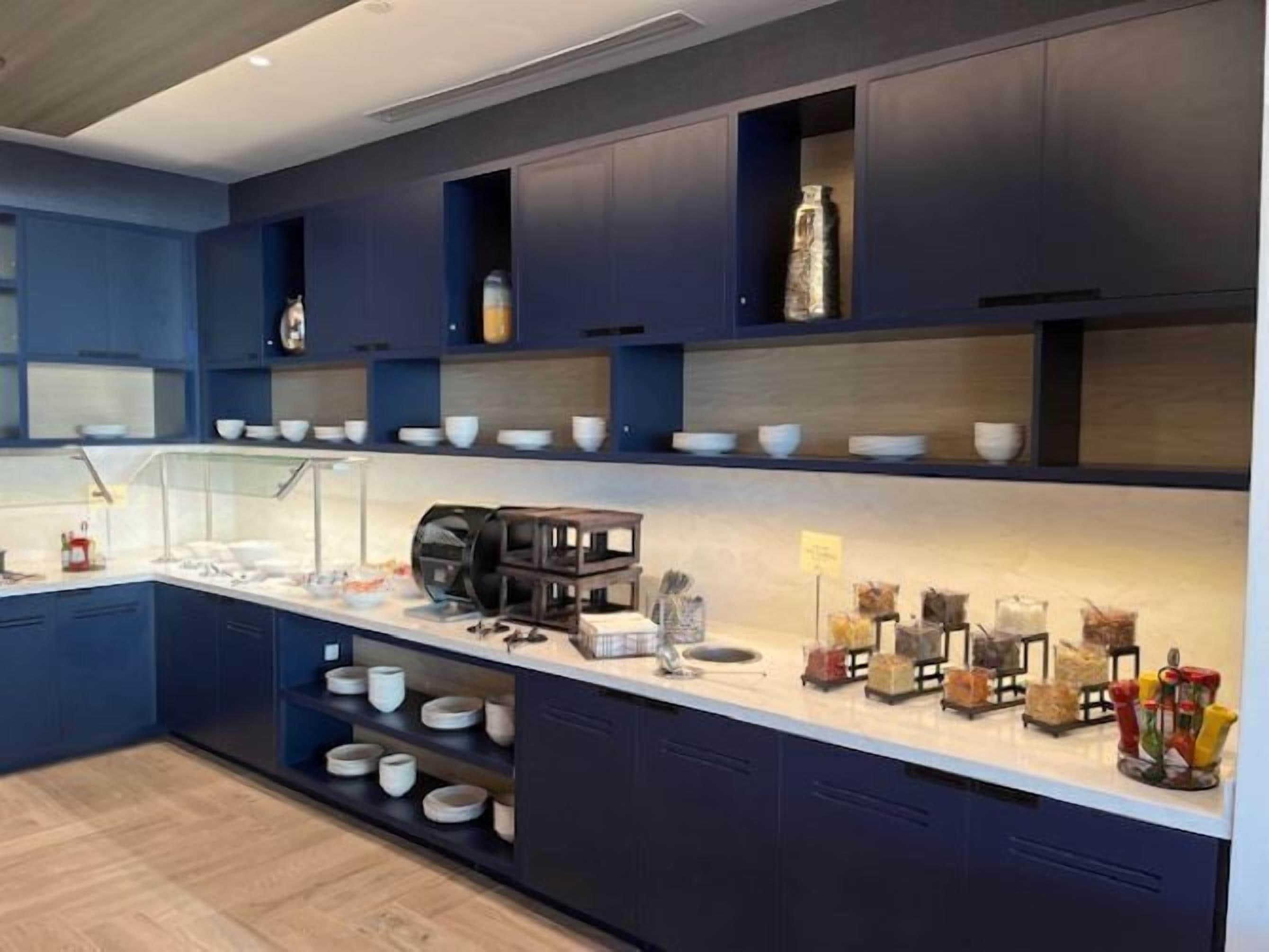 Una cocina moderna con armarios azul oscuro, encimeras blancas y diversos electrodomésticos y utensilios de cocina.