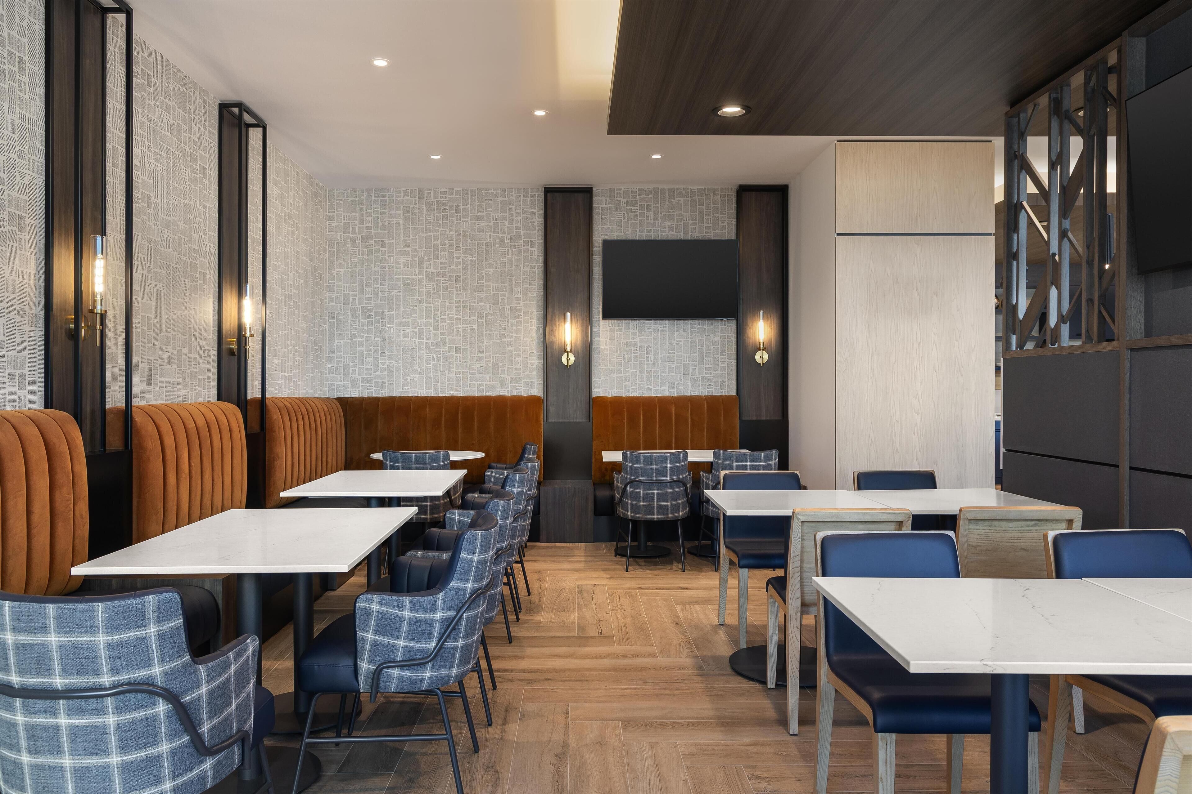 A modern dining area with booths and tables, wooden flooring, and wall-mounted lighting.