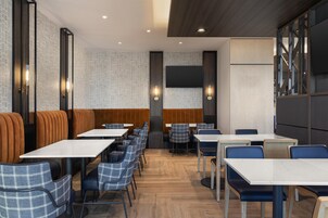 Een moderne eetruimte met zitjes en tafels, houten vloeren en wandlampen.