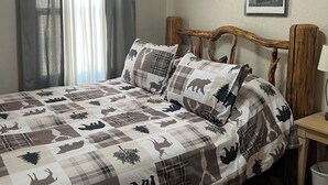 Une chambre à coucher avec un lit, des rideaux, une tête de lit, une table de chevet, une lampe et deux tableaux encadrés accrochés au mur.