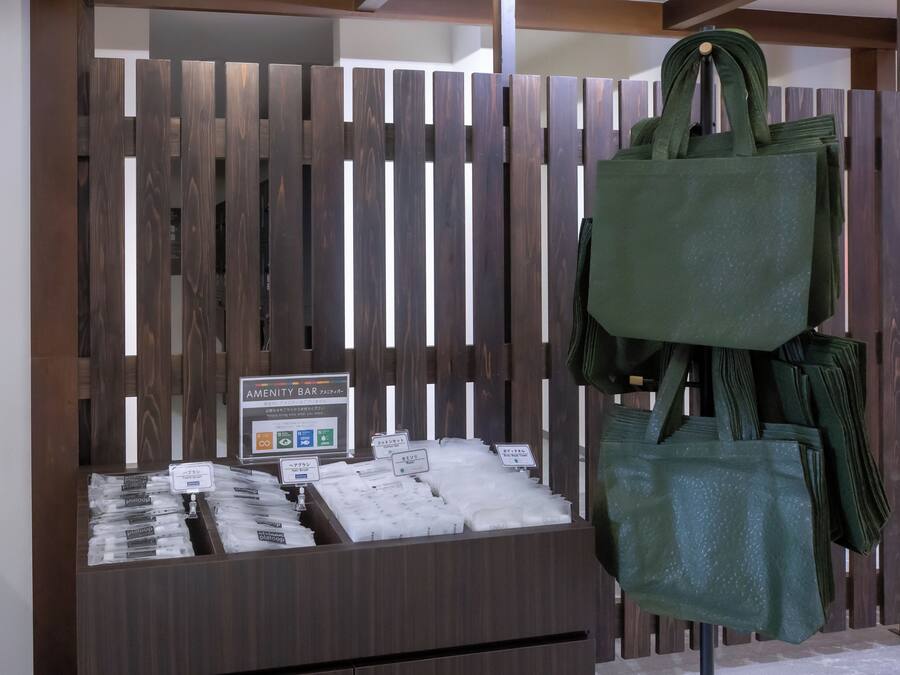 A wooden partition with a sign for an amenity bar, a display of packaged goods, and a green tote bag hanging on the partition.