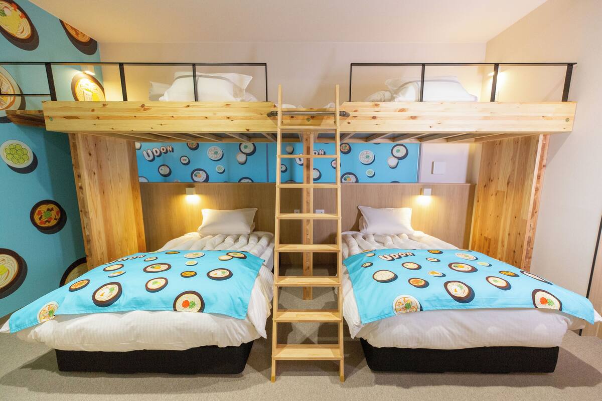 Ein Schlafraum mit Etagenbett, einer Leiter, zwei Betten mit blau-weißer Bettwäsche und einer Wand mit kreisförmigen Mustern.
