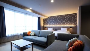 A modern hotel room with a sofa, a bed, a coffee table, and a large window with curtains.