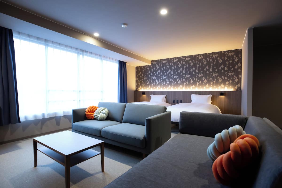 Ein modernes Hotelzimmer mit einer Couch, einem Bett, einem Couchtisch und einem großen Fenster mit Vorhängen.