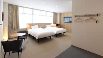 Une chambre d’hôtel avec deux lits, une petite table ronde et une chaise. Il y a deux écrans de télévision fixés au mur et un porte-manteau avec des cintres.