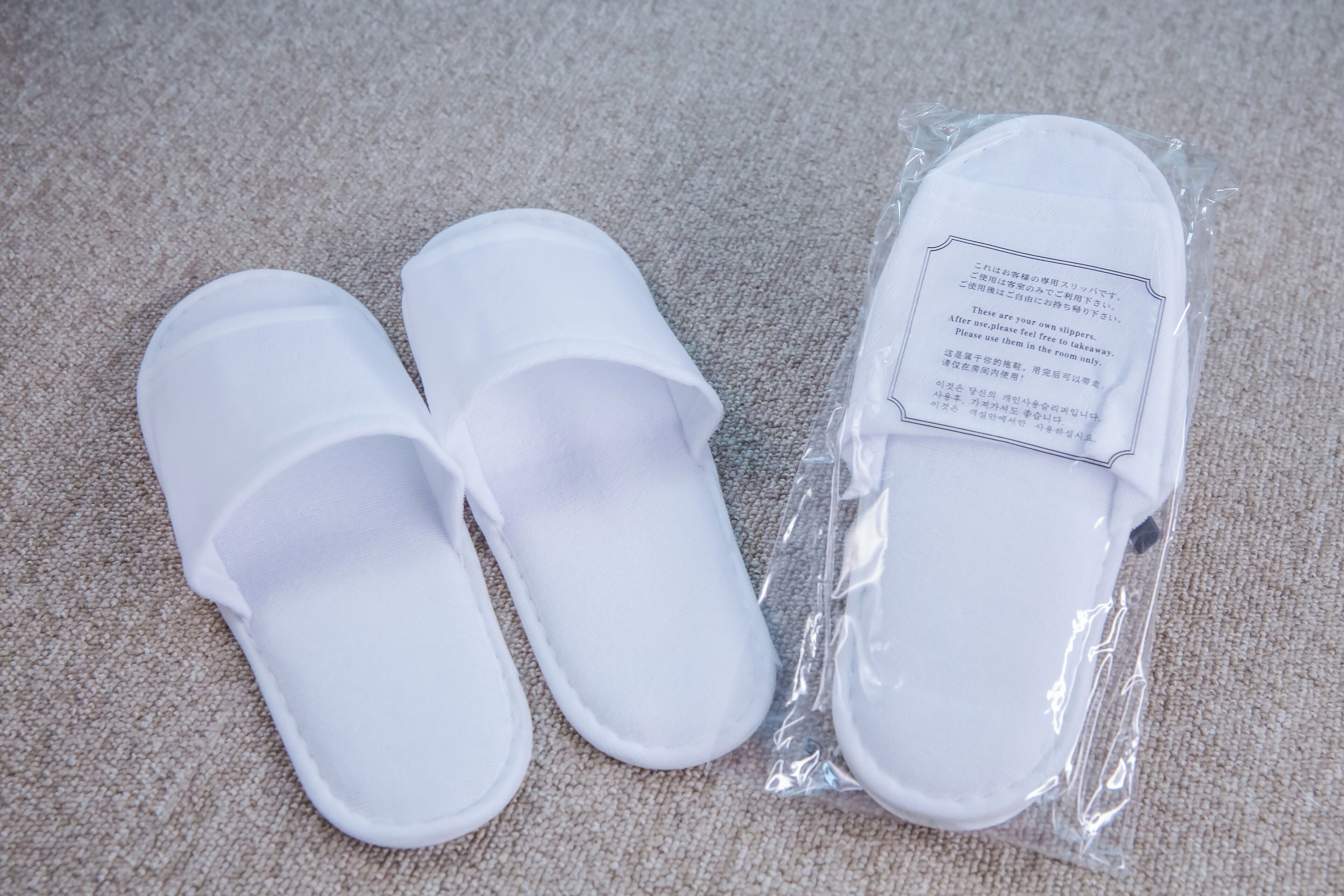Twee witte pantoffels en een plastic verpakking met tekst erop.