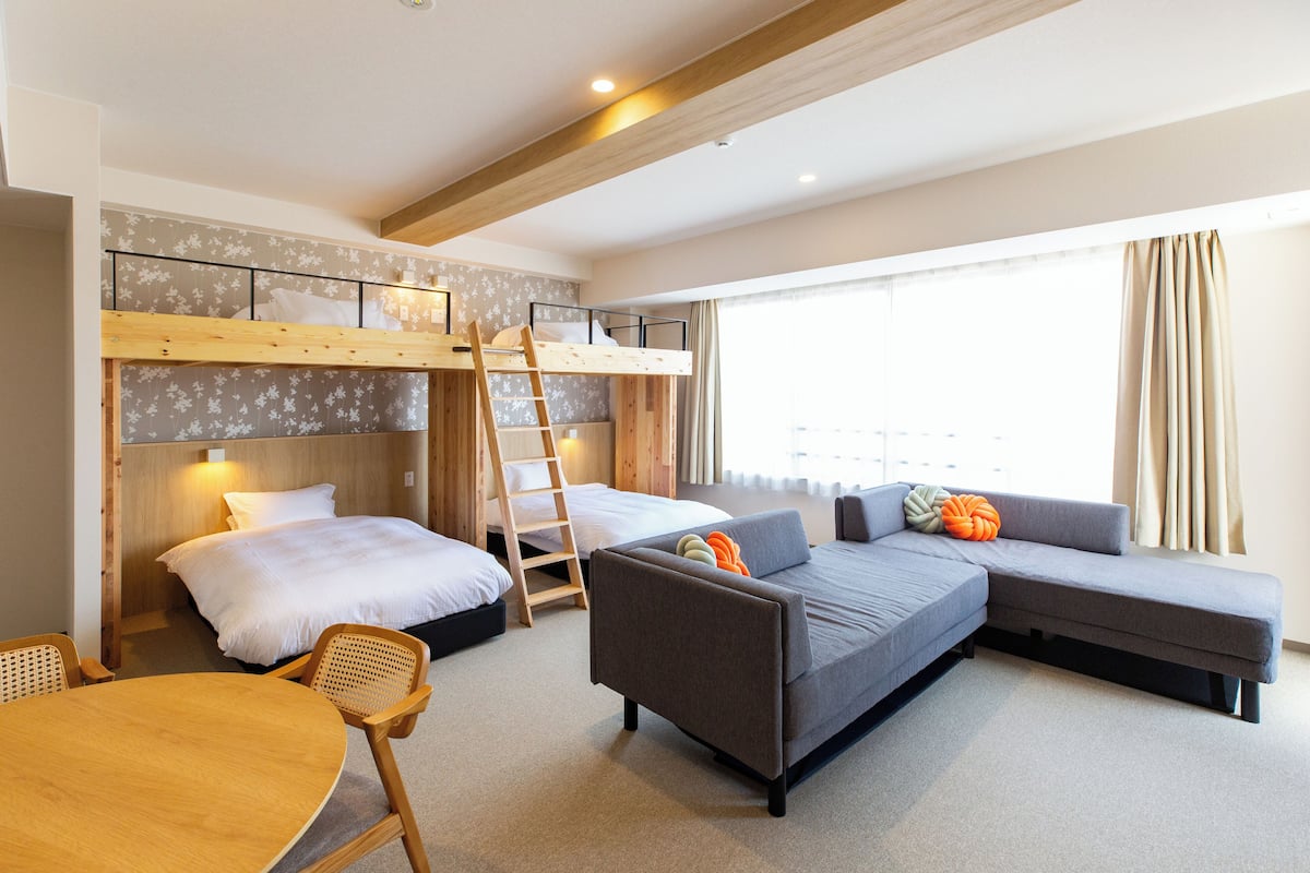 Ein Zimmer mit einem Etagenbett, einer Schlafcouch, einem Esstisch und einer Treppe.