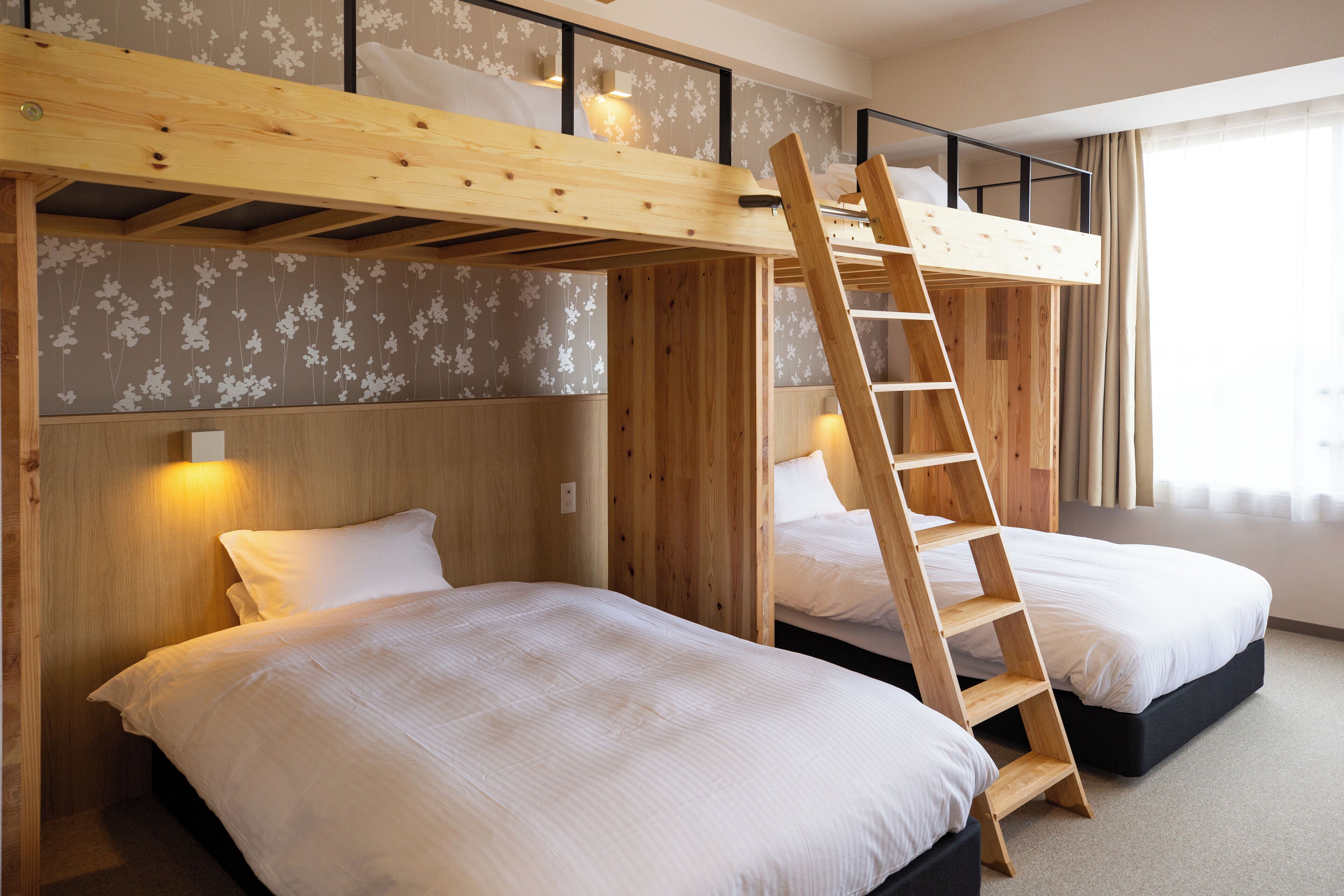 Una habitación con dos camas, cabeceros de madera, una escalera y un papel tapiz con motivos florales.