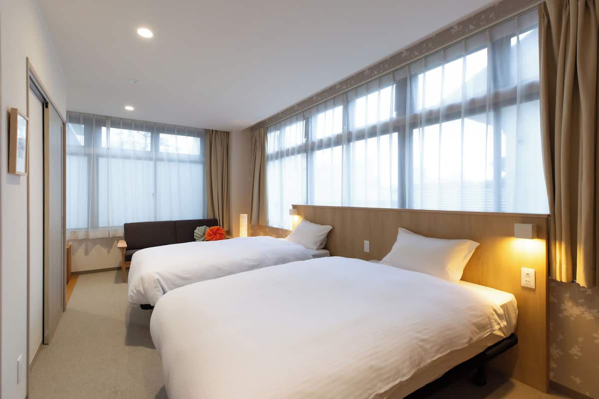 Ein Hotelzimmer mit zwei Betten, einem Sofa und großen Fenstern mit Vorhängen.