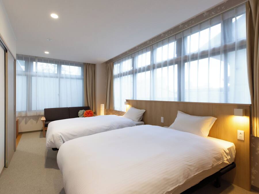 A hotel room with two beds, a sofa, and large windows with curtains.