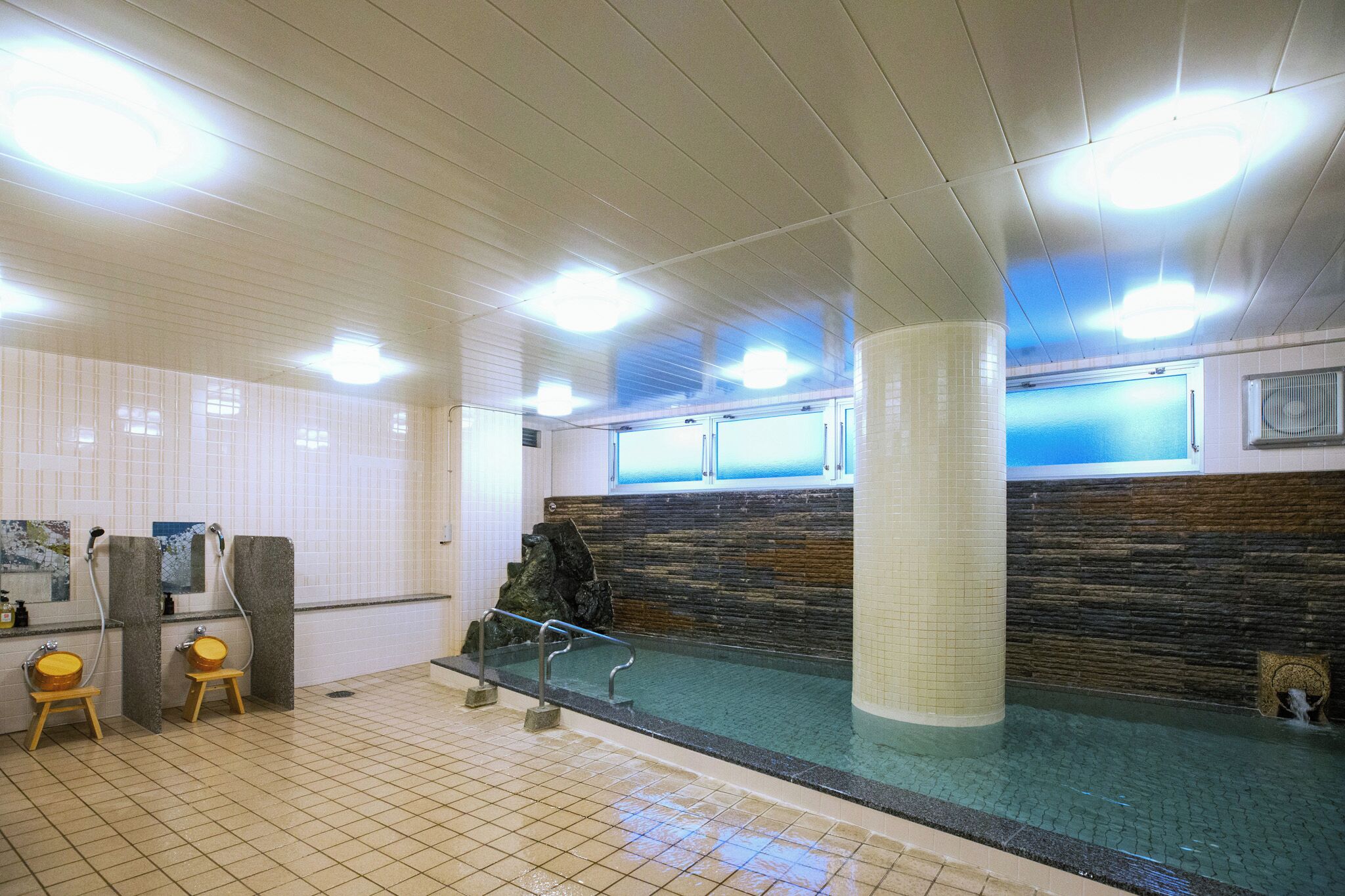 A public swimming pool with tiled walls, a central column, and a bench.