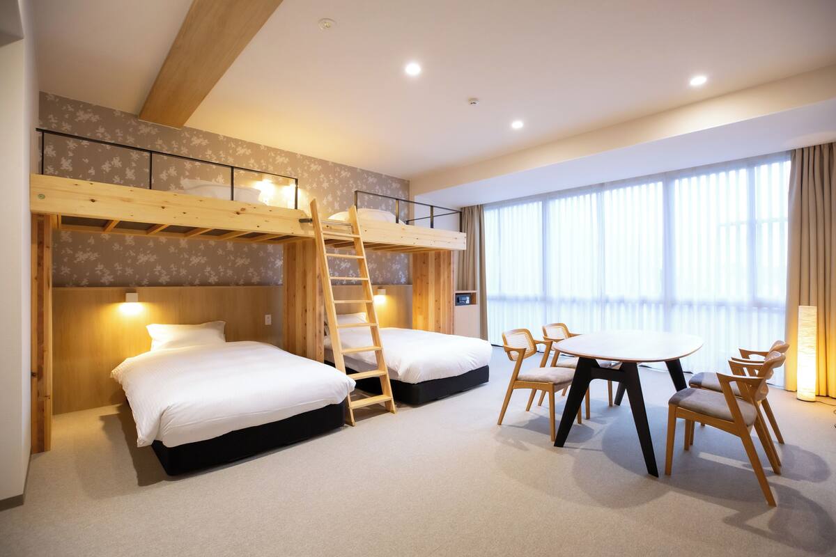 Ein Hotelzimmer mit Stockbetten, einem Schreibtisch, Stühlen und einem großen Fenster.
