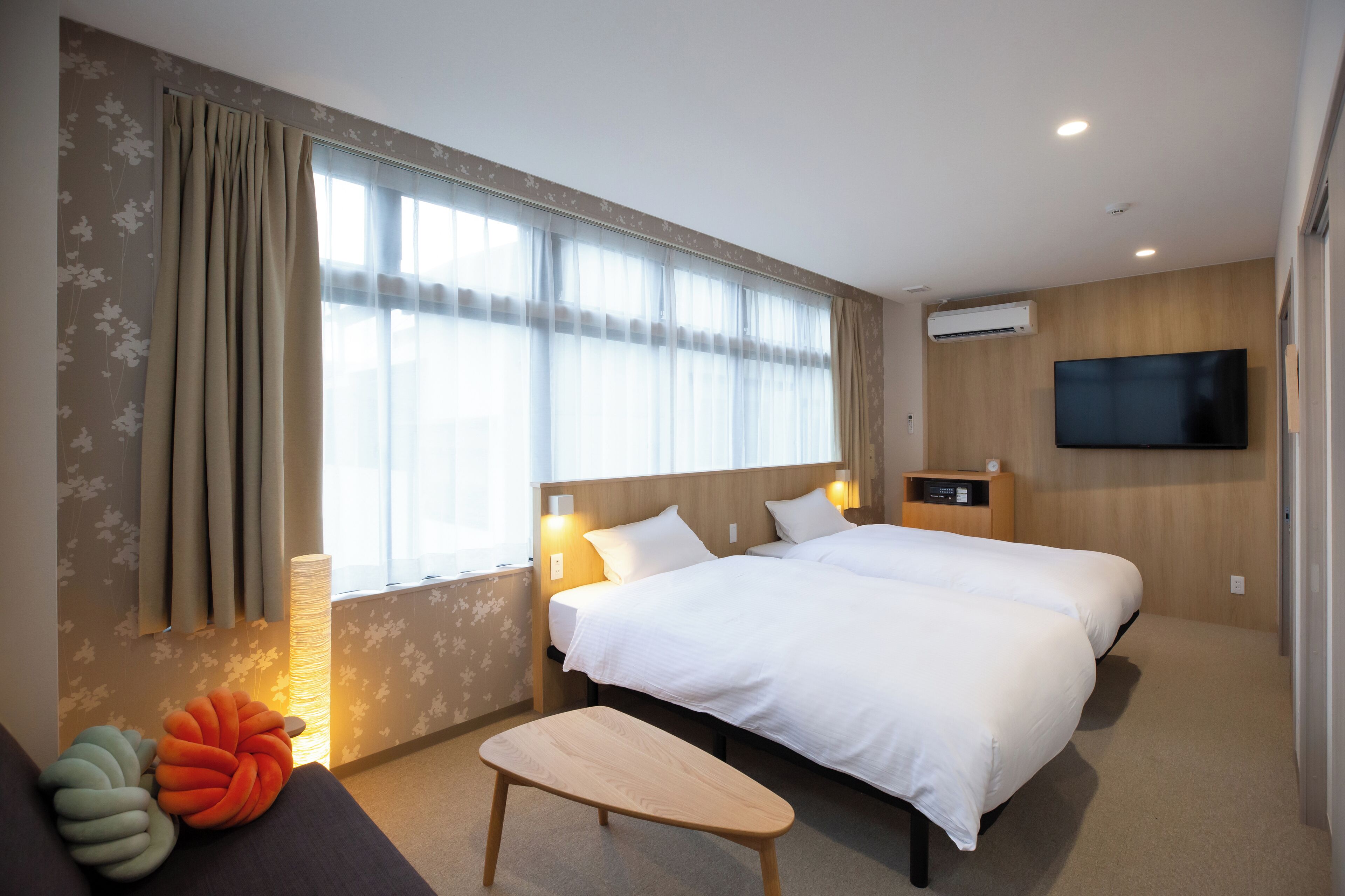 Een hotelkamer met twee bedden, een flatscreen televisie aan de muur, een nachtkastje met een lamp en een raam met gordijnen.