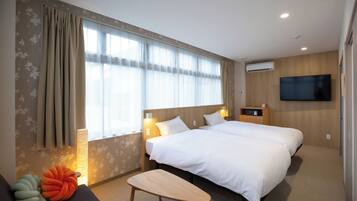Een hotelkamer met twee bedden, een flatscreen televisie aan de muur, een nachtkastje met een lamp en een raam met gordijnen.