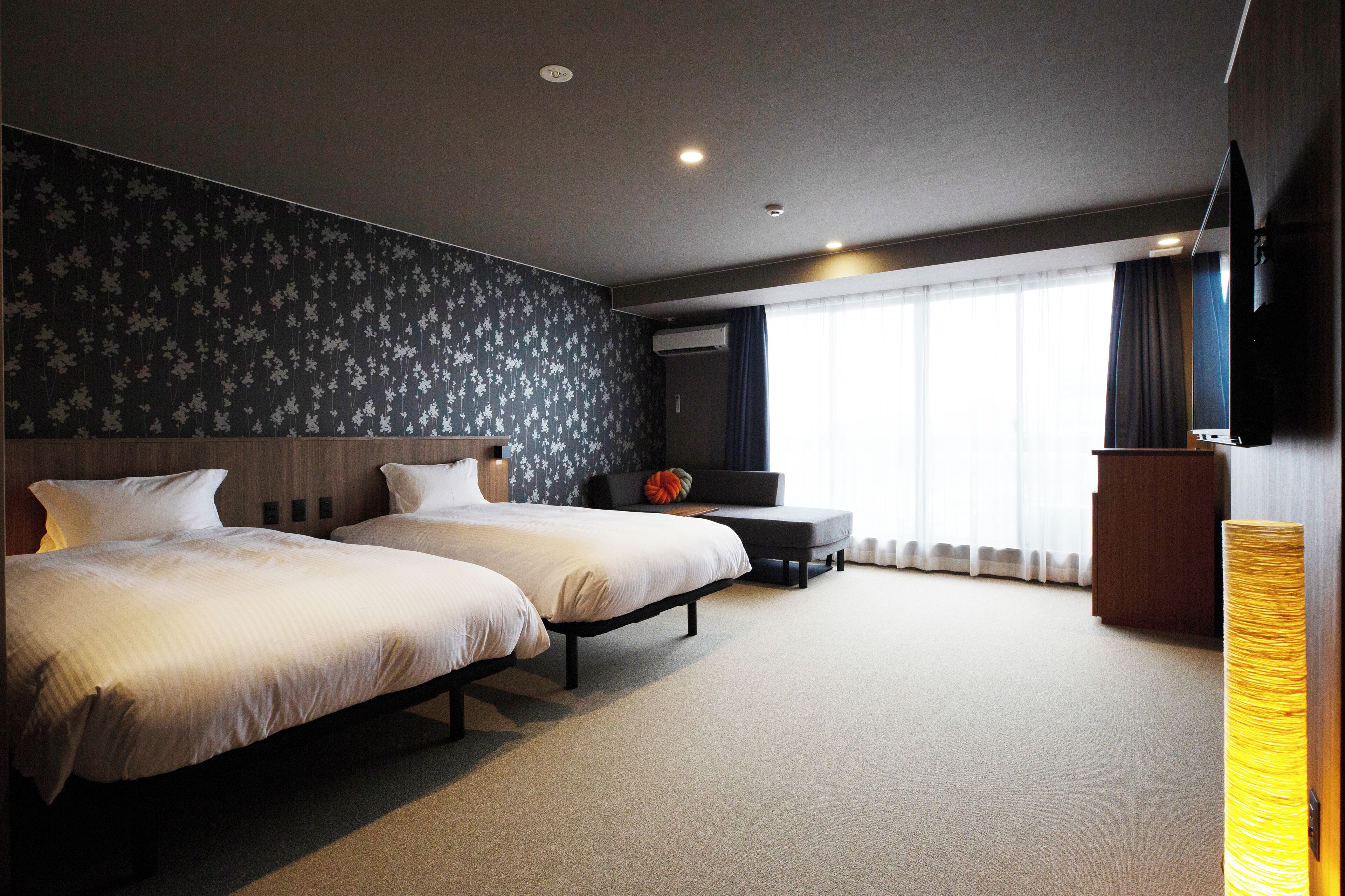 Une chambre d’hôtel avec deux lits, un bureau, une chaise et une grande fenêtre avec des rideaux.