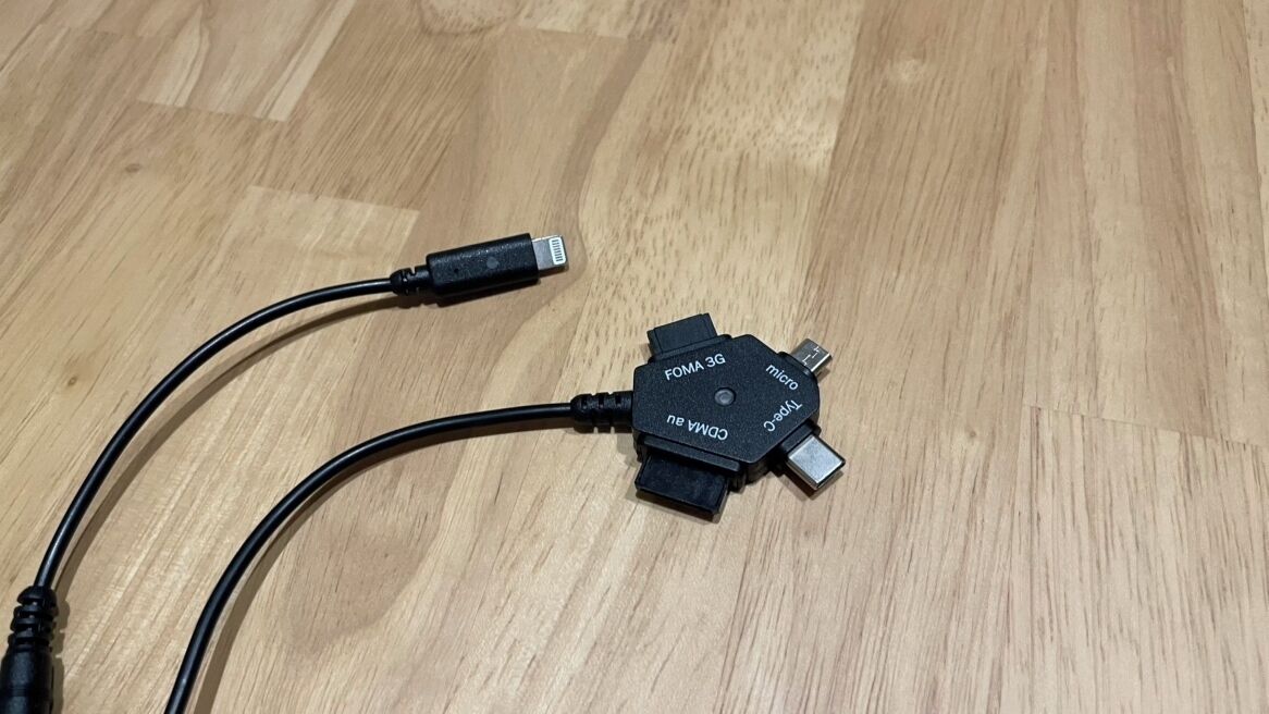 Ein USB-C-Kabel, verbunden mit einem schwarzen FOMA 3G-Mikro-USB-Adapter, liegt auf einem Holzboden.