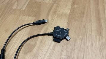 Ein USB-C-Kabel, verbunden mit einem schwarzen FOMA 3G-Mikro-USB-Adapter, liegt auf einem Holzboden.
