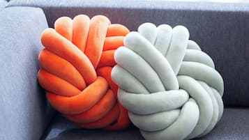 Two knitted poufs in orange and white colors placed on a grey sofa.