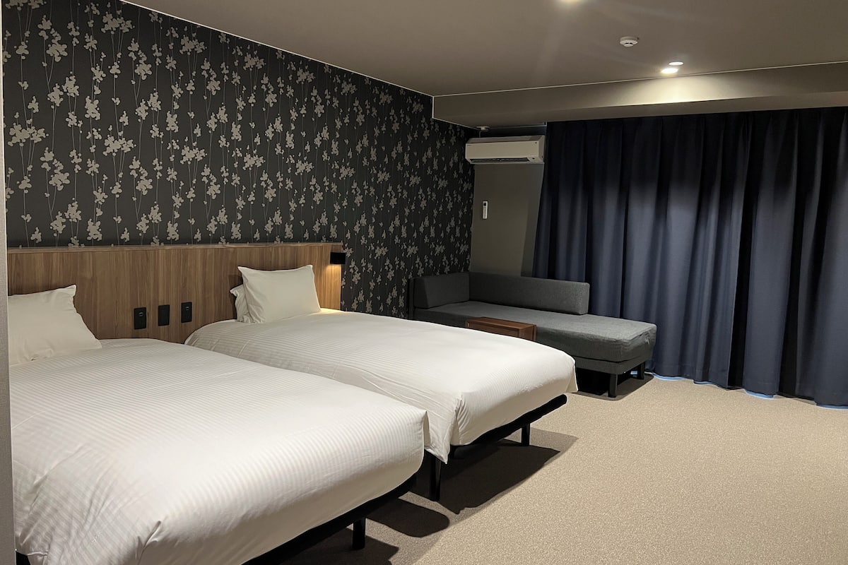 Ein Hotelzimmer mit zwei Betten, einem Sofa, einem Spiegel und einem Fenster mit Vorhängen.