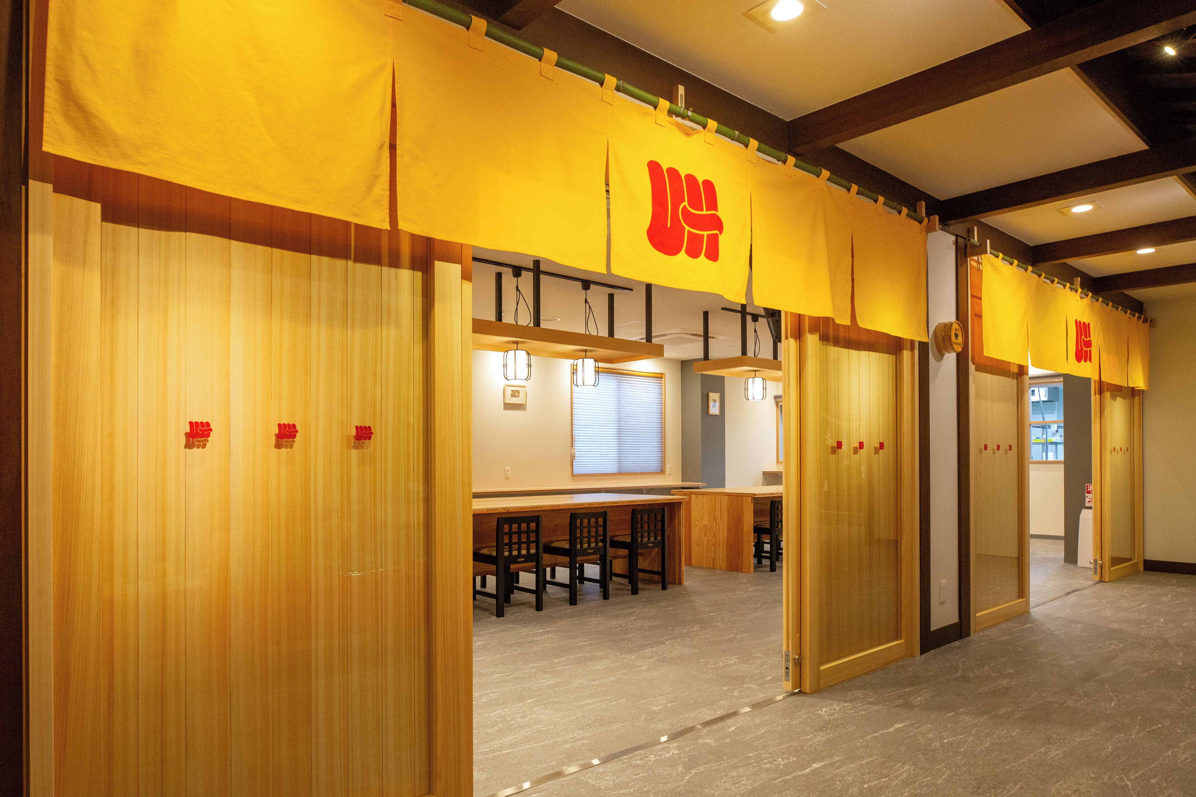 A hotel lobby with wooden flooring, a reception desk, and sliding doors with red signage.