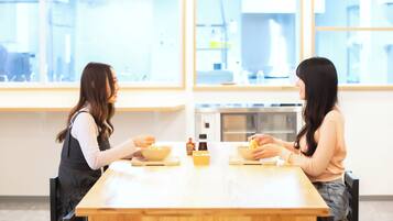Dos personas sentadas en una mesa de madera en una habitación luminosa con ventanas amplias.