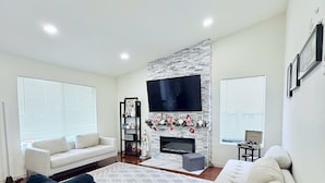 A modern living room with a fireplace, white sofas, a blue bean bag, and a flat-screen TV mounted on a brick wall. - Garden vibes - 3BR Home near Downtown (San Jose)